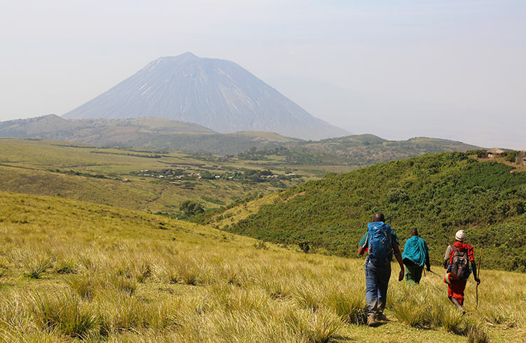 Hiking guides, including an armed ranger and a local Maasai, approach Lengai volcano in Tanzania.