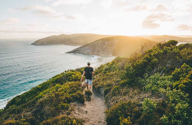 A man hikes a sandy trail along the Australia coast.