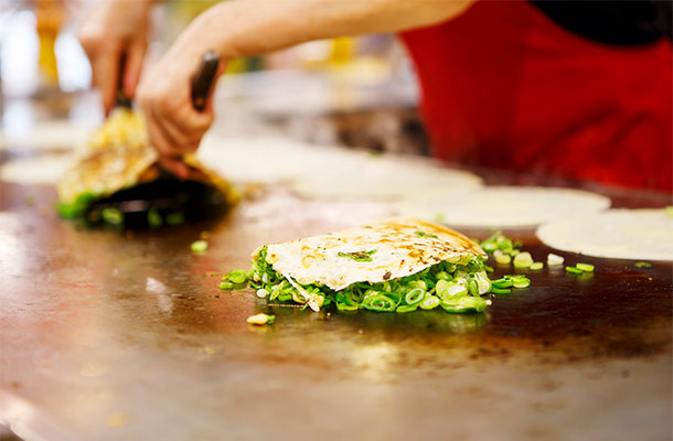 Okonomiyaki being cooked on a grill.