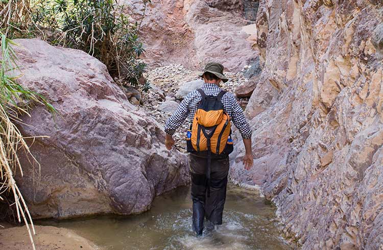 A hiker wades through a river in Jordan, near Petra.