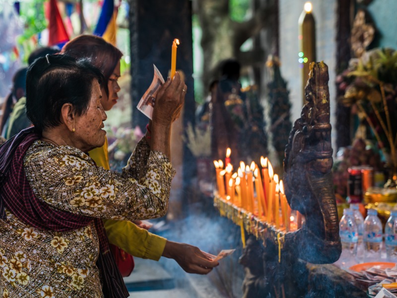 Cambodian woman at local temple lights a candle during prayer.