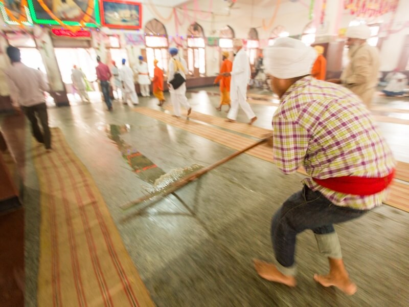 A boy cleans the floor of the langar between a quick turnover of meals. 