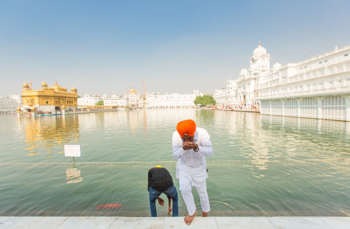 Sikh men dip their hands to drink the holy water said to hold blessings that purify karma. 