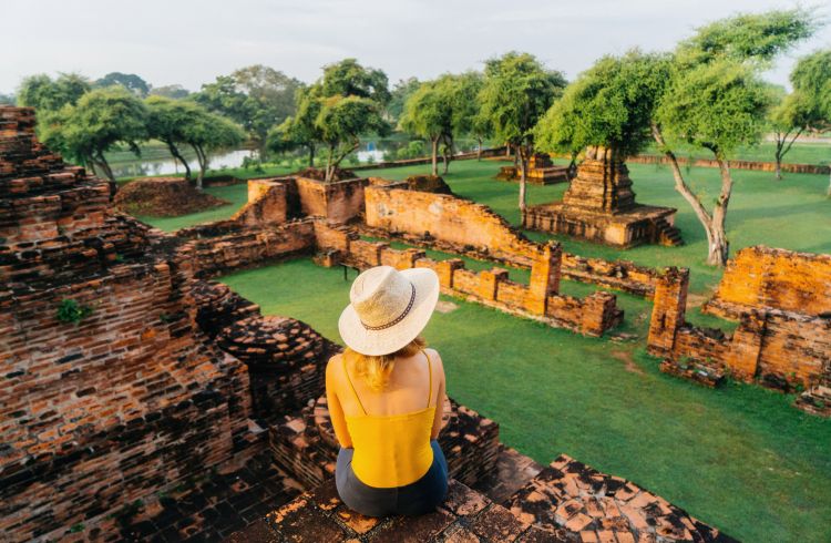 A young woman sitting near the ruins of ancient Buddhist Temple, Ayutthaya, Thailand