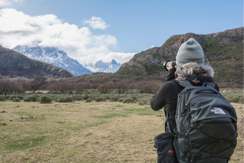 A woman photographing a snow capped mountain
