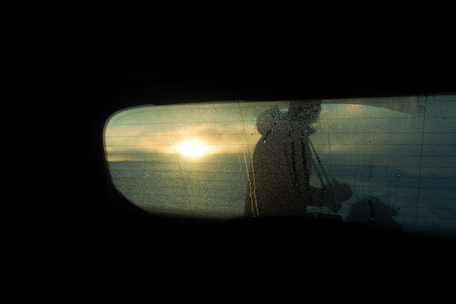 A person walking in front of the sun, seen through the back of a car