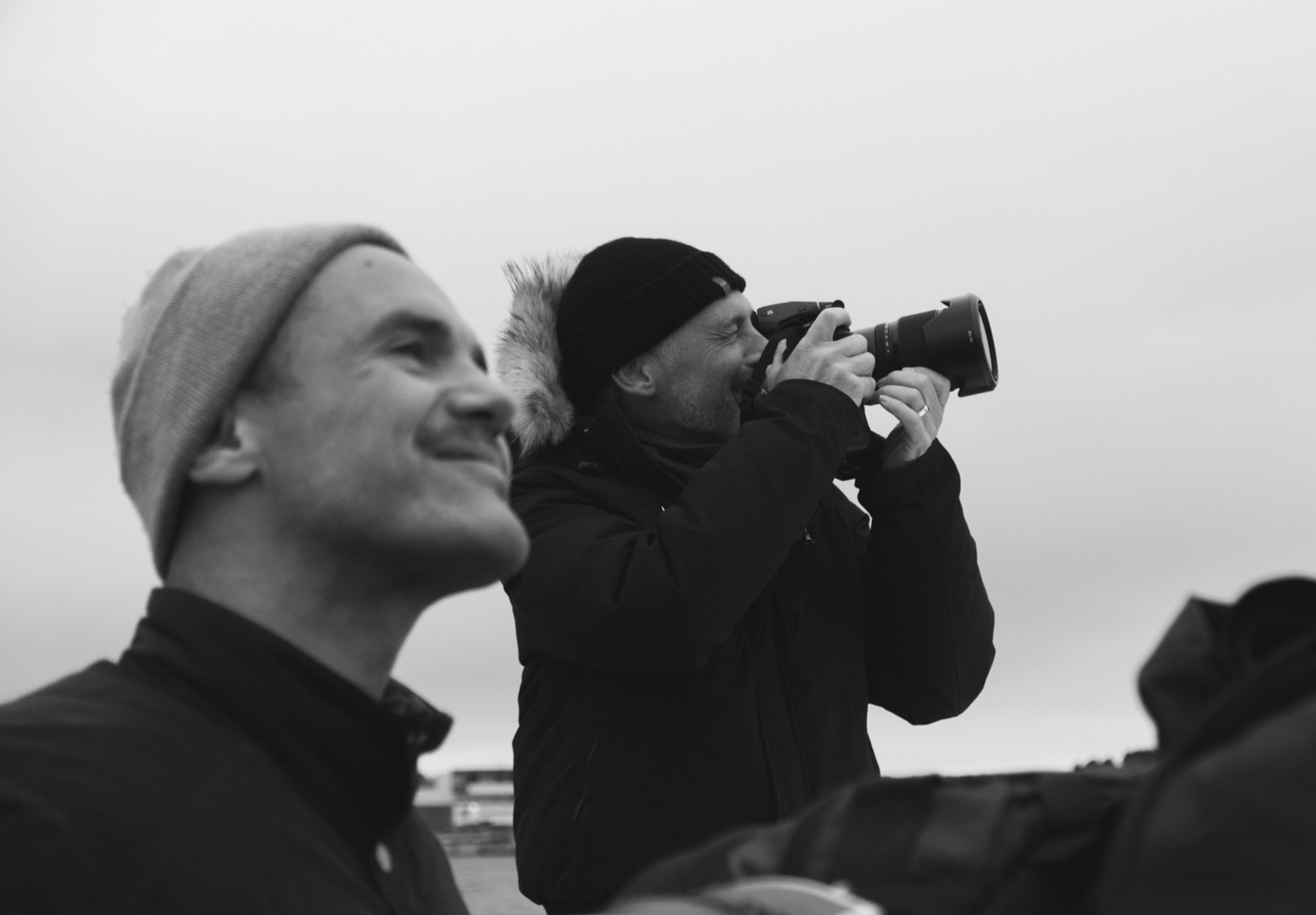 Two men smiling, one looking through a camera lense