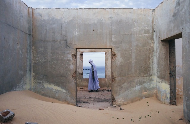 a local Mauritanian draped in violet, walking past a doorway