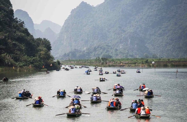 Many boats rowing down a river with mountains in the background