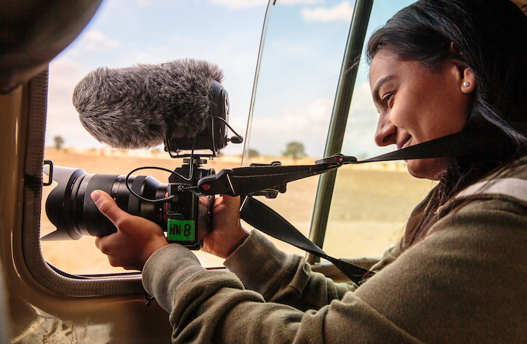 A filmmaker with a camera and microphone films from a car.