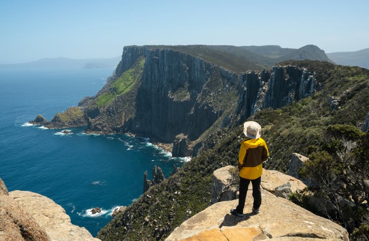 A hiker looks out over dramatic seacliffs along the Three Capes Track in Tasmania.
