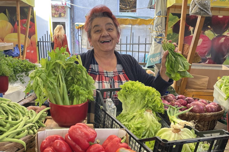 A smiling woman selling vegetables at a market in Bosnia and Herzegovina.