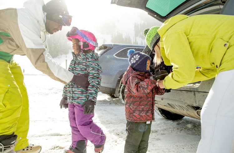 A mixed-race couple in ski attire dress their small children for a day on the slopes.