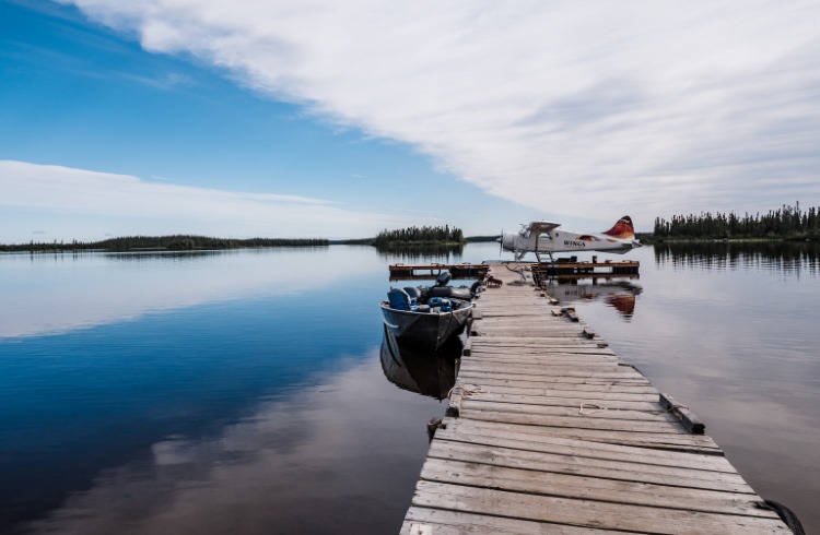 A float plane is moored by a jetty on a mirror-calm lake in Manitoba, Canada.