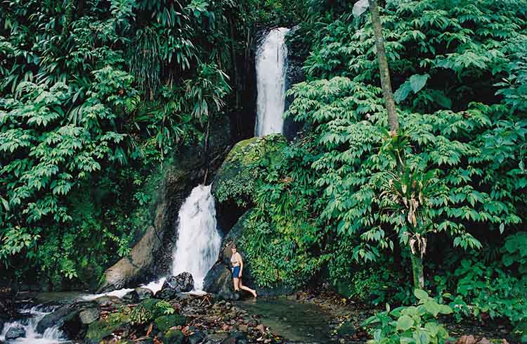 A young woman hiking near the base of a waterfall in Dominica.
