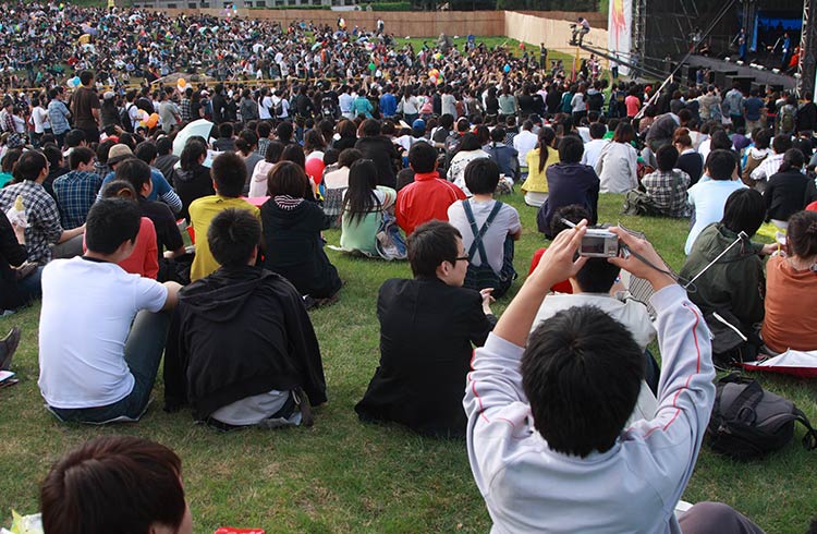 A huge crowd gathers on a lawn to see a concert in China
