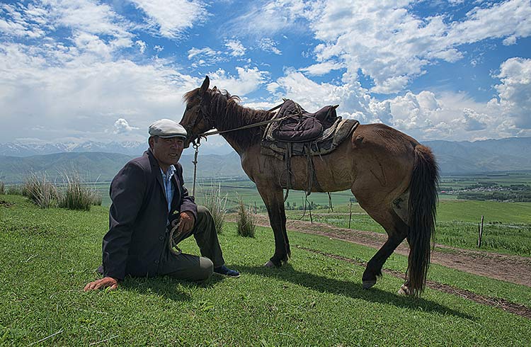 A man sits on the grass with his horse in Xinjiang Province