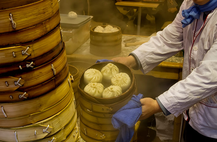 A chef holds a bamboo container filled with Chinese soup buns