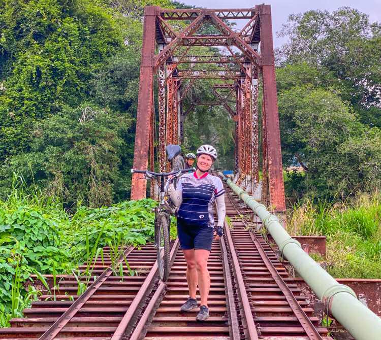 A woman poses with her mountain bike on an abandoned railroad bridge in Costa Rica.