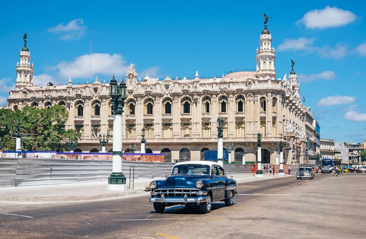 A classic car passes in front of an ornate historic building in Havana, Cuba.