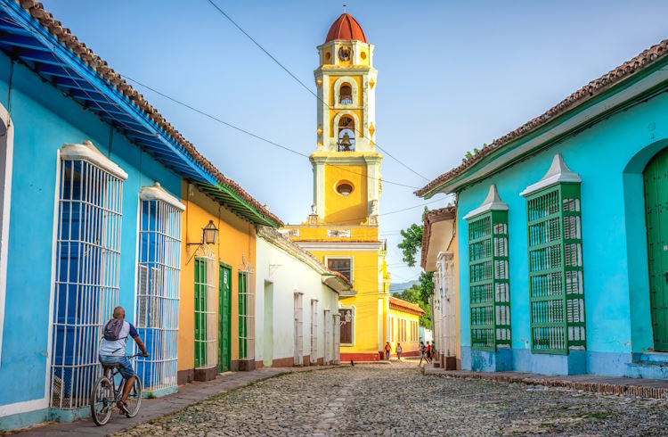 A man cycles down a cobbled street lined with pastel-colored buildings in Trinidad, Cuba.