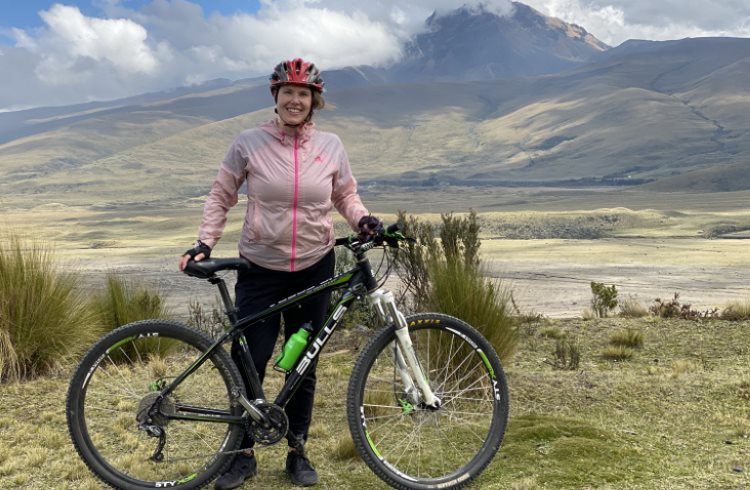 A woman stands next to her mountain bike in front of the Cotopaxi volcano in Ecuador.