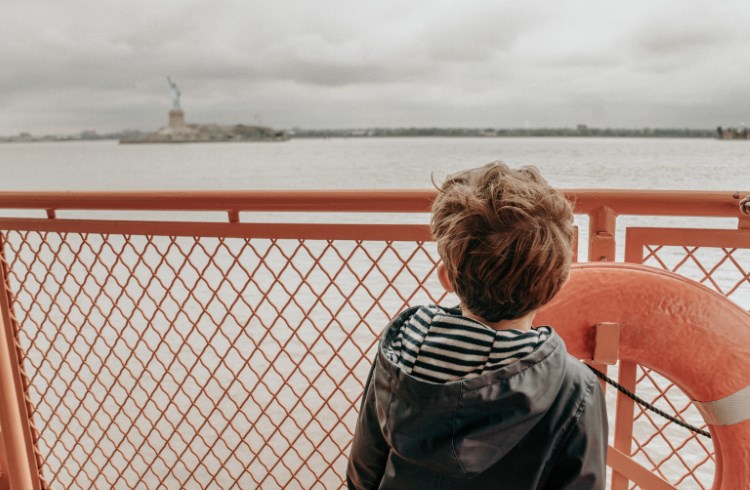 A young boy aboard the Staten Island Ferry looks across the harbor at the Statue of Liberty.