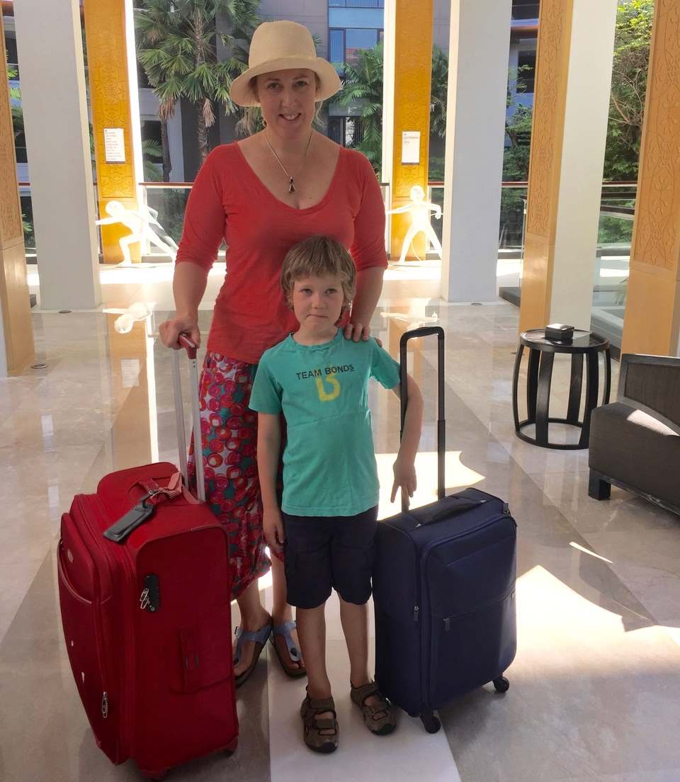 A mother and son stand with their luggage in a hotel lobby in Bangkok.