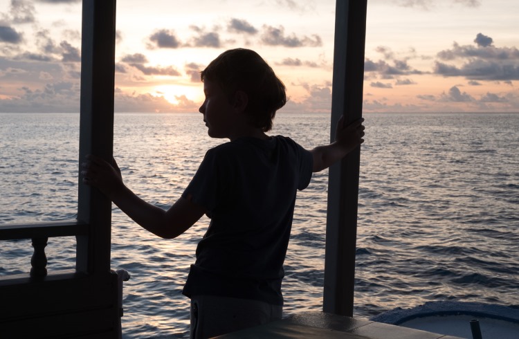 A young boy looks across the water from an oceanside patio in the Maldives.