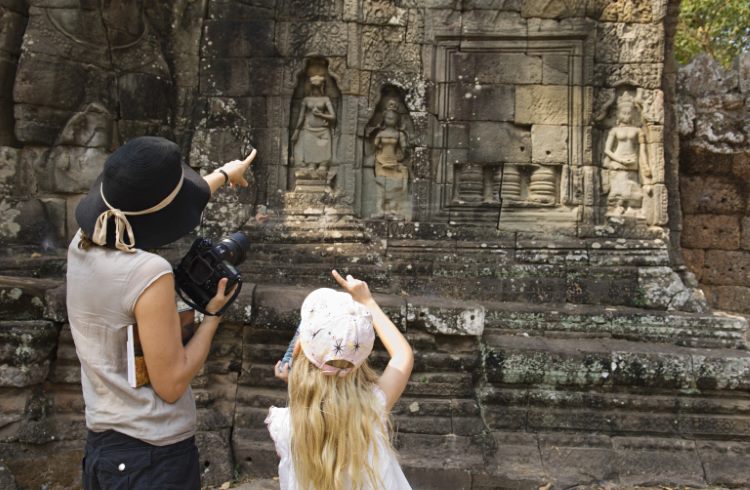 A mother stands with her daughter, pointing out details of a ruined temple in Siem Reap, Cambodia.