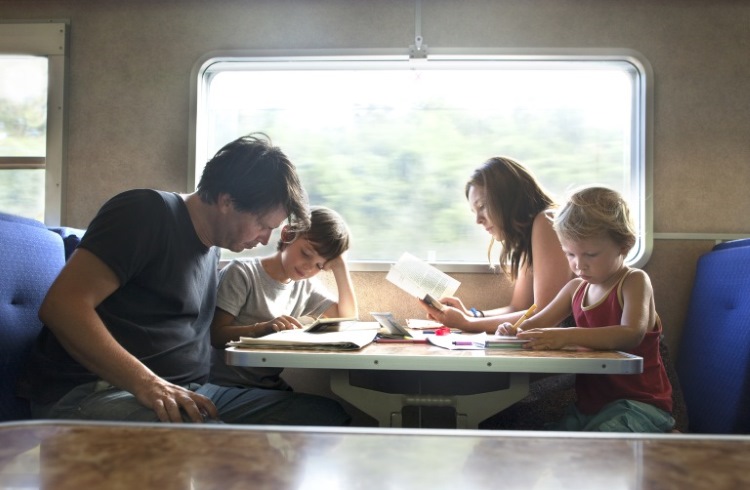 A family sits on a moving train, poring over travel-planning materials.