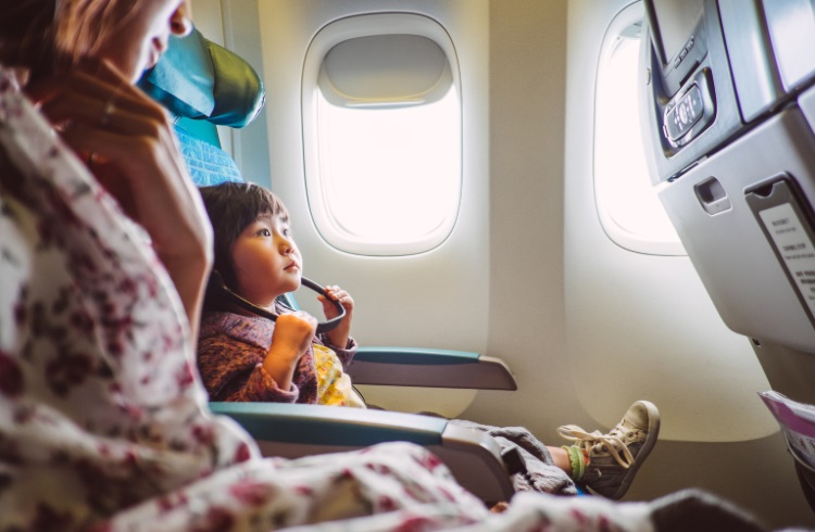 An Asian woman and her toddler watch a movie aboard an airplane. 