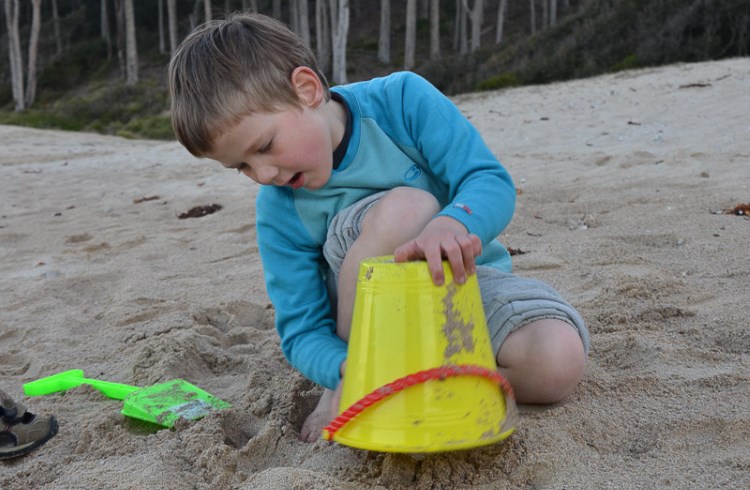 A young boy dumps sand from a bucket on a beach in Australia.