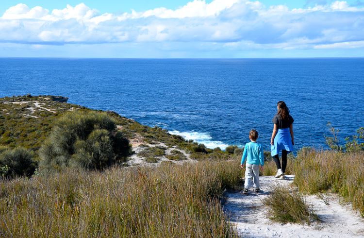 An 11-year-old girl and her younger brother look out over a blue ocean from a sandy bluff in Australia.