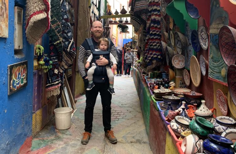 A father stands in a pottery market in Fes, Morocco, holding his young son in a baby carrier.