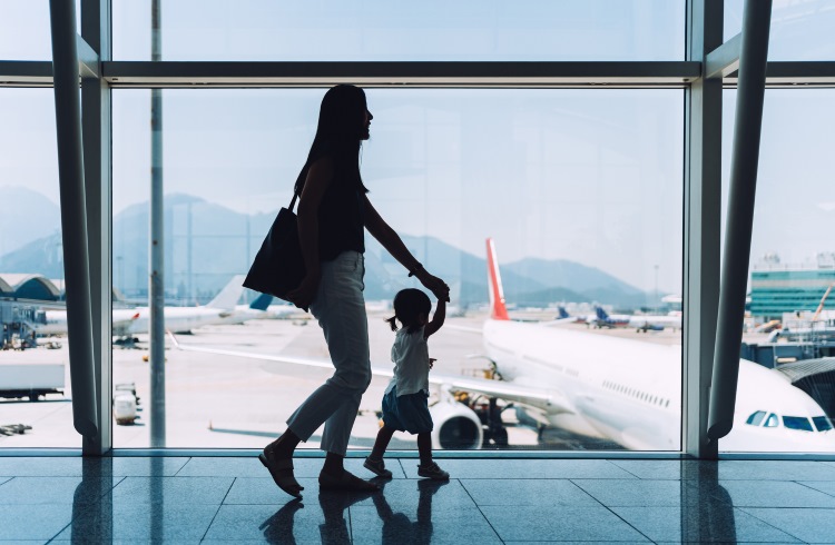 An Asian woman walks past an airport window with her toddler.