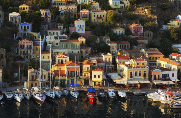 Colorful buildings rise above a turquoise harbor in Symi, Greece.