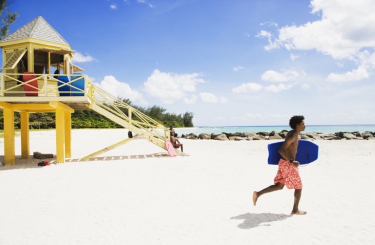 A man runs along a beach in Barbados carrying a boogie board.