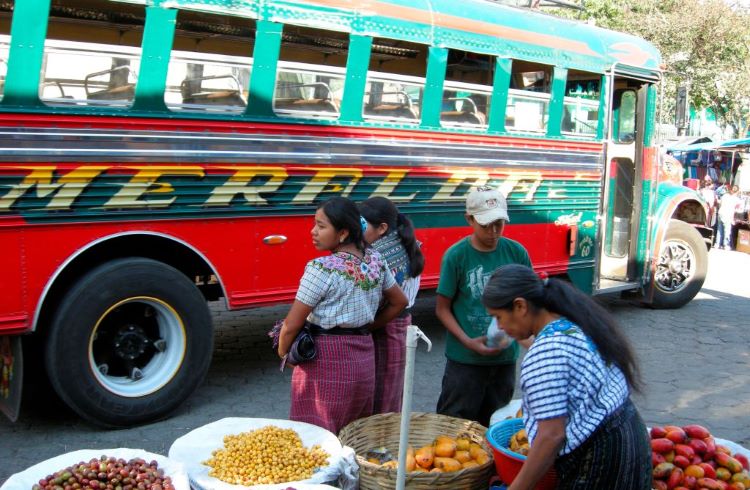 A woman sells fruit in front of a colorful bus in Lake Atitlan, Guatemala.