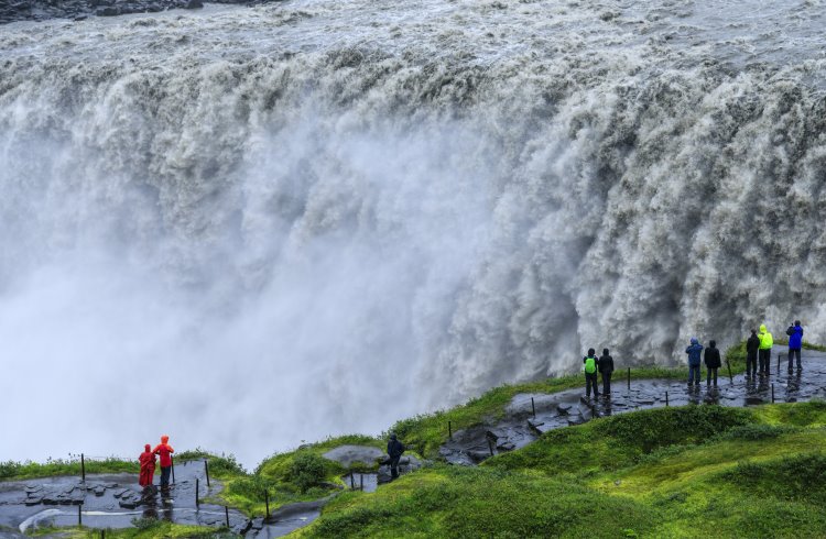 A group of people stand in front of the raging waters of Dettifoss, Iceland's most powerful waterfall.