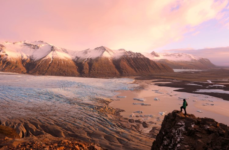 A hiker stands on a cliff overlooking Skaftafell Glacier in Iceland.