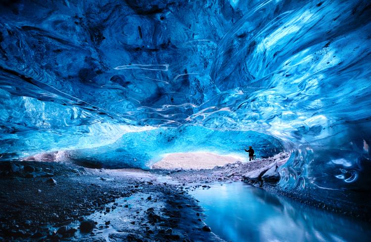 A man stands at the entrance to an ice cave beneath Vatnajökull Glacier, Iceland.