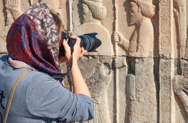 A woman traveler in a headscarf takes photos at the ancient ruins of Persepolis, Iran.