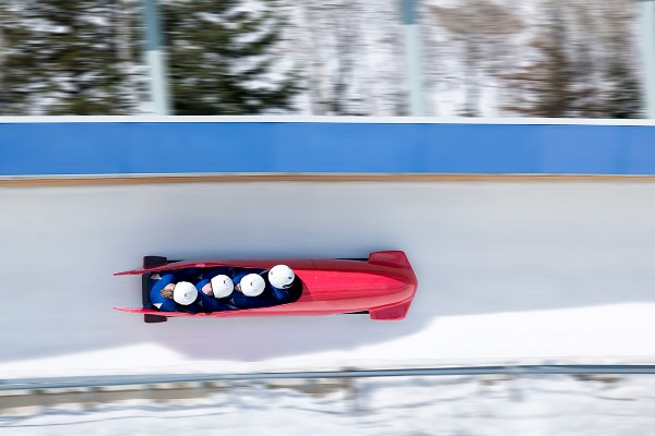 Four men bobsled racing down track, view from above (blurred motion)
