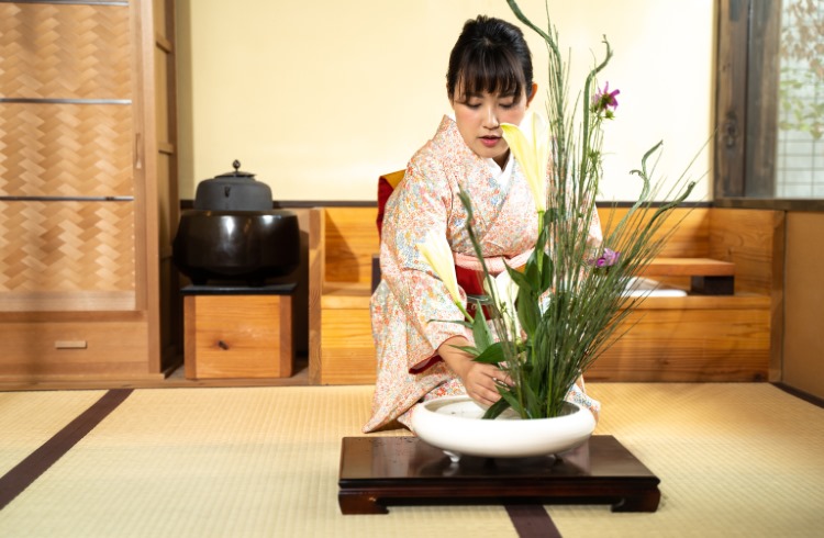 A Japanese woman in a kimono arranges flowers in the Ikebana style.