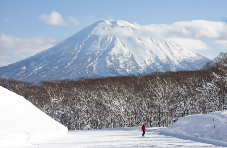 A snowboarder on a slope with a view of Mt Yotei in Niseko, Hokkaido, Japan.