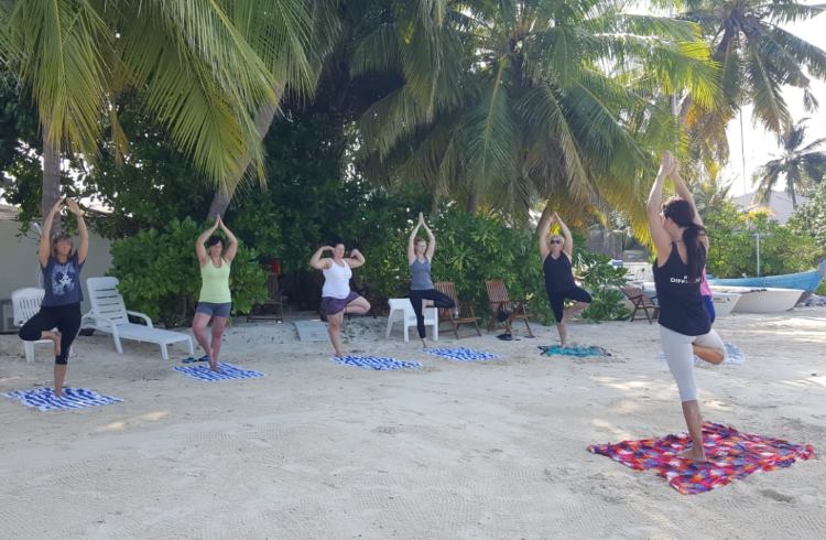 A group of women do yoga on a beach in the Maldives.