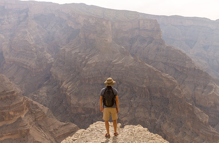 Standing on the edge of a cliff overlooking the canyon below, in Oman.