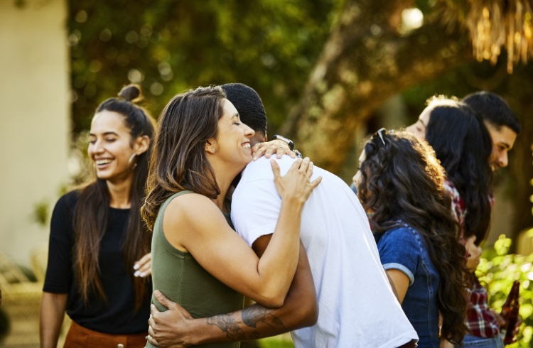 At an outdoor gathering, a group of young adults greets each other with hugs.
