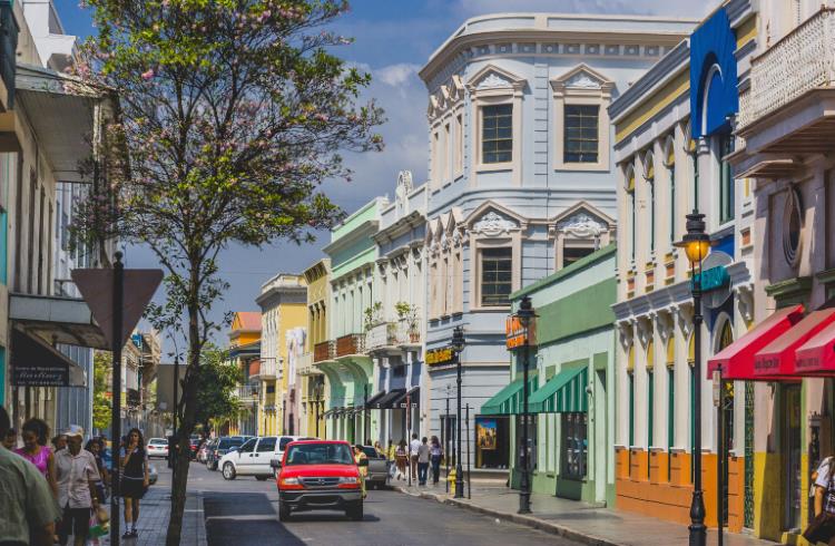 A car drives down a street lined with colorful buildings in the city of Ponce, Puerto Rico.